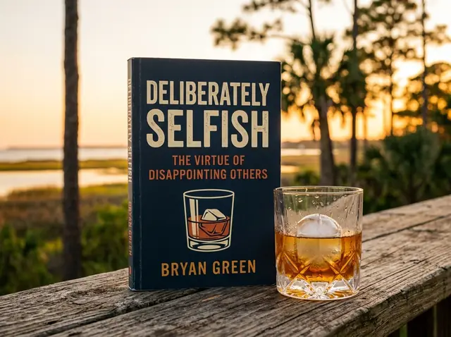 A paperback copy of Deliberately Selfish by Bryan Green standing on a weathered porch table beside a glass of bourbon, longleaf pines and salt marsh behind it at golden hour.